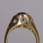 Gold signet style ring with large central purple sapphire, engraved with stars and comets, some set with diamonds.  Standing view wide side 1