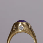 Gold signet style ring with large central purple sapphire, engraved with stars and comets, some set with diamonds.  Standing view alternate wide side