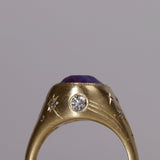 Gold signet style ring with large central purple sapphire, engraved with stars and comets, some set with diamonds.  Standing view alternate wide side