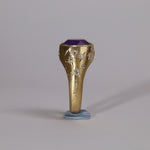 Gold signet style ring with large central purple sapphire, engraved with stars and comets, some set with diamonds.  Standing view narrow side 1