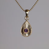 Gold teardrop pendant with a purple gemstone on a gray background