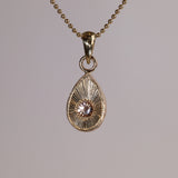 Gold teardrop pendantt with a pink and peach stone on a grey background.