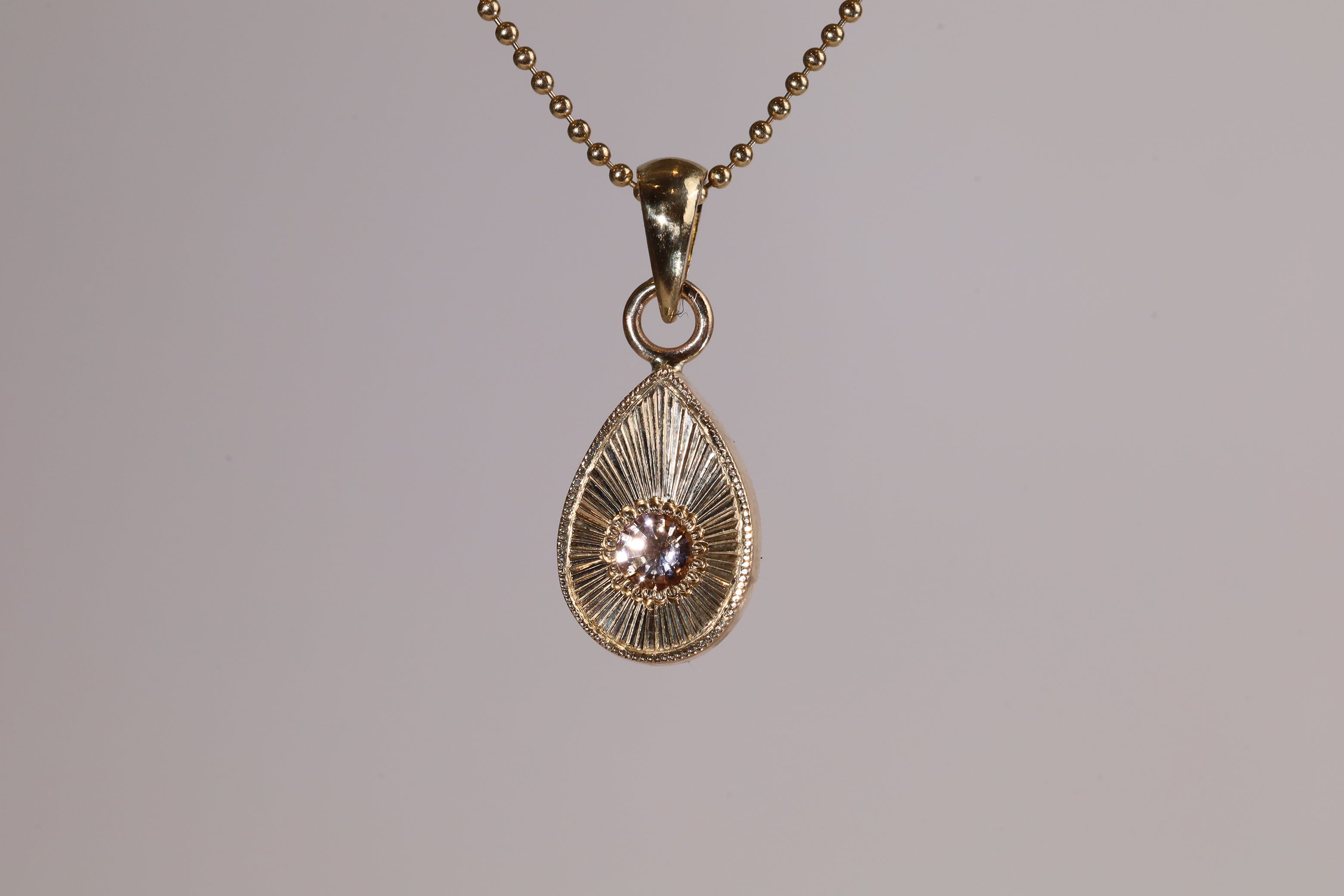 Gold teardrop pendantt with a pink and peach stone on a grey background.