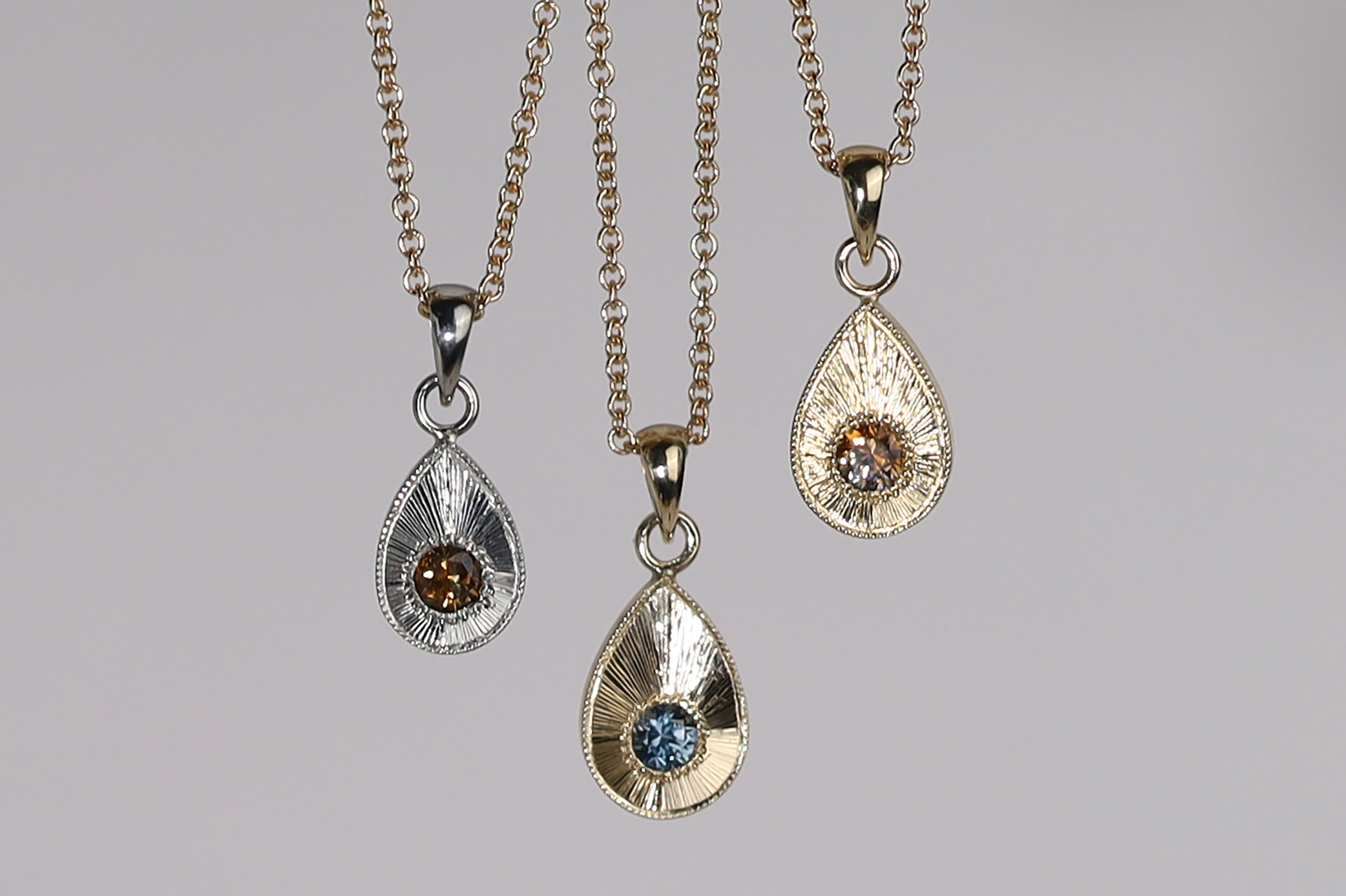 Trio of plume charms on chains, which feature a tear drop shape with engraved rays emanating from central gem stone.