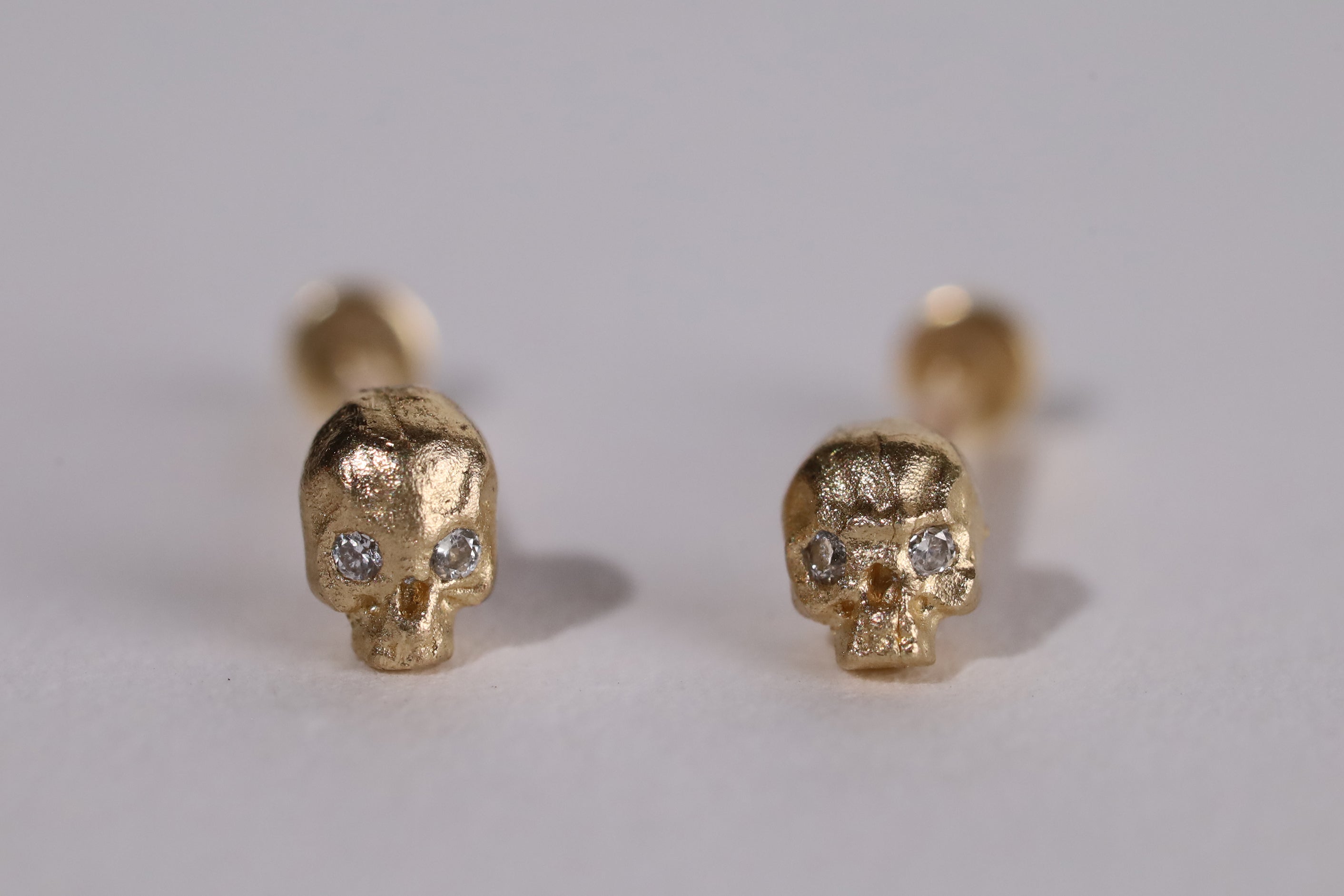 Pair of yellow gold cast skull studs with diamond set eyes.